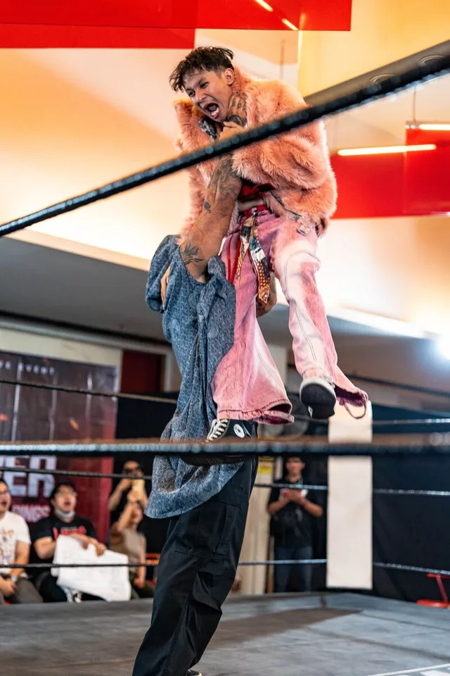 A wrestler in a pink fur coat is hoisted mid-air